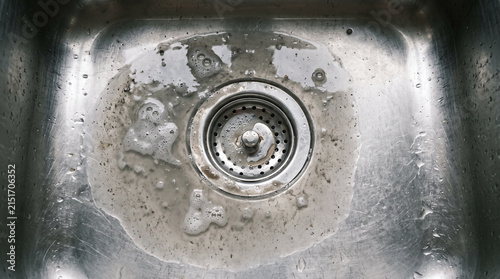Standing soapy grey water pooling around a stainless steel kitchen sink drain