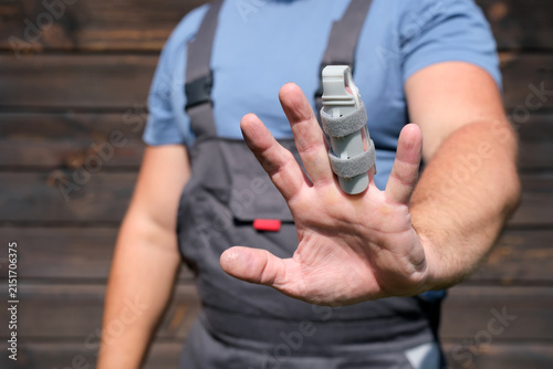 Fotografie Worker in protective workwear with injured finger wearing a splint, occupational