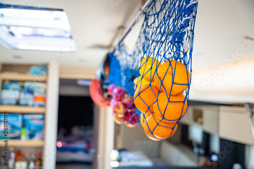Bild auf Leinwand Fresh oranges and other citrus fruits stored in a hanging net inside a yacht galley during a sailing trip