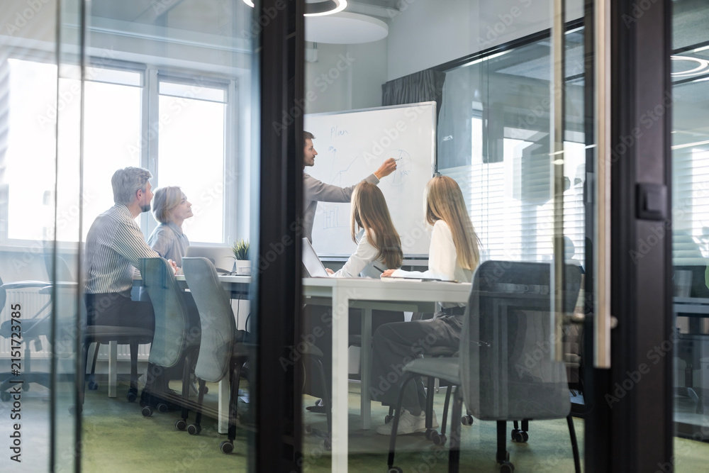 Obraz premium A modern office interior, featuring a blurred view of workers at desks, through a glass partition.
