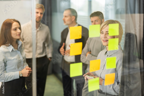 Businesspeople talking in their diverse team during a brainstorming session with sticky notes on glass wall in a modern office