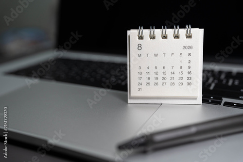 August 2026 small desk calendar on laptop workspace with pen on office table. business scheduling, time management, event planning, deadline tracking, work efficiency, and corporate organizing.