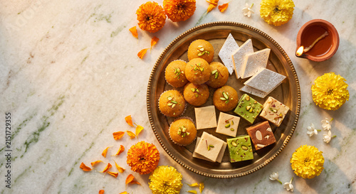 Assorted Indian sweets and traditional mithai arranged on a brass plate with marigold flowers and diya for festive celebration