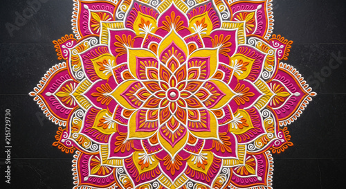 Bright floral rangoli mandala with pink, yellow and orange patterns on dark floor for Indian festival decoration and cultural celebration
