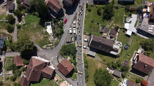 Forward top-down drone footage showing a large herd of cows filling the main road of a Swiss village as the animals descend from the surrounding Alps.