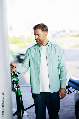 Man fueling car with a green nozzle at a gas station and paying contactless using his smartphone