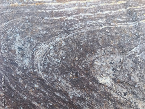 Natural rock surface with layered mineral patterns, rough weathered texture, and earthy gray and brown tones. Organic stone background for architecture, construction and interior design