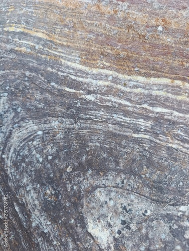 Natural rock surface with layered mineral patterns, rough weathered texture, and earthy gray and brown tones. Organic stone background for architecture, construction and interior design