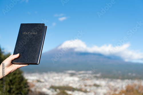 Foto A hand holds a black, hardcover Holy Bible aloft with the iconic snow-capped Mount Fuji and Fujinomiya city in the background, from the Shirao Mountain Park (Shiraosan), Japan