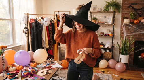 Woman in witch hat holding pumpkin in cozy room.