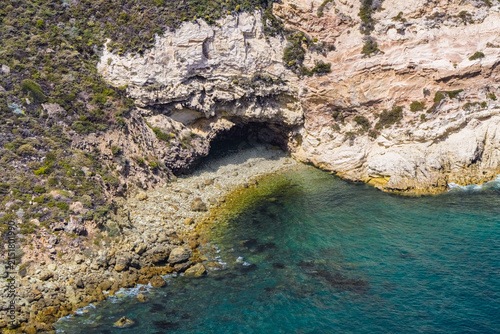 Konstfotografi Rocky cove with a shadowed sea cave, boulder strewn beach and clear turquoise sh