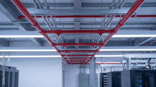 Фотография Bright red fire suppression system pipes and white linear lighting fixtures mounted on the ceiling of a modern data