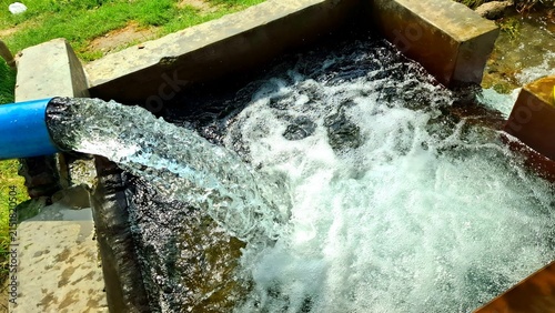 Fotografie Fresh water flowing from a blue pipe into a concrete reservoir tank for irrigati