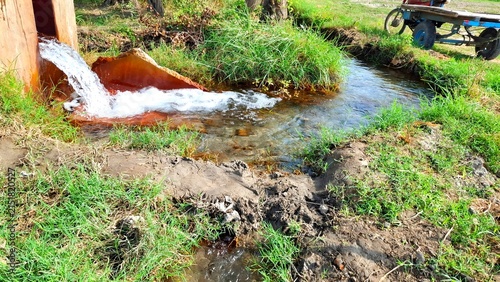 Принти на полотні Fresh water flowing from a pipe into a rural irrigation ditch in a green field