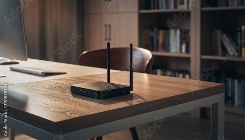 Wireless router with two antennas on a wooden desk in a study room.