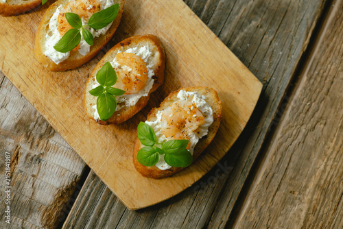 Photography Bruschetta or crostini with cream cheese, shrimp garnished with fresh basil on wooden board