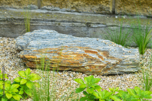 Photography Large decorative natural stone boulder placed in a modern garden landscaping design, surrounded by small gravel and green plants, tranquil outdoor rockery and zen garden background