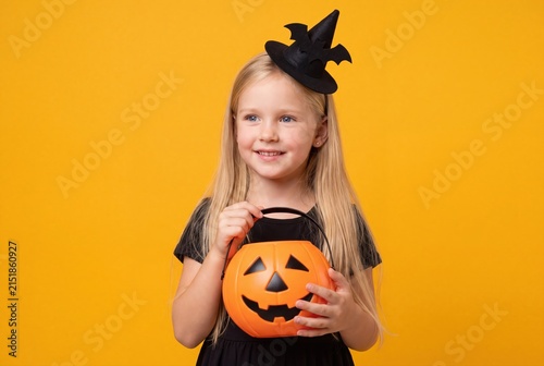 Little girl in witch hat holding a pumpkin candy bucket for Halloween