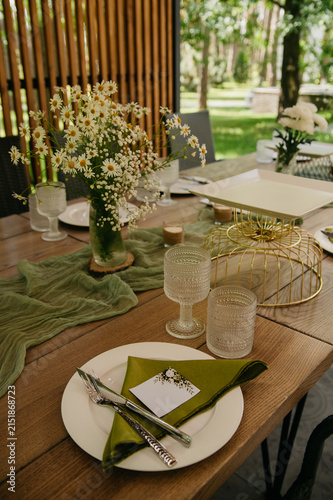 Banquet table in a restaurant for a wedding or anniversary celebration with served dishes, flowers in vases, napkins, ladles, spoons and glass glasses