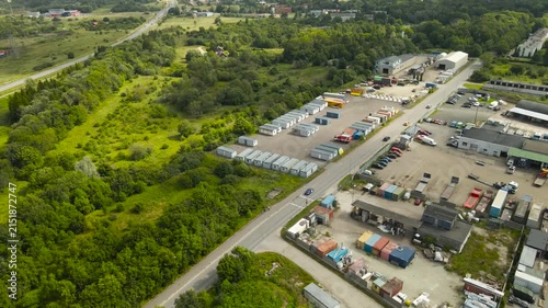Industrial warehouse and logistics park next to a lush green forest, showing a stark contrast between nature and industry with cars driving on a road separating the two distinct zones