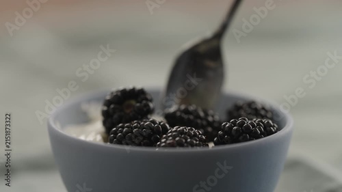 Slow motion taking a spoon of blackberries with yogurt from a bowl