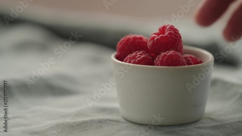 Slow motion man hand put fresh ripe raspberries in a white small bowl