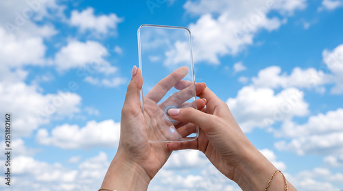 Hands holding a transparent smartphone with a clear screen against a bright blue sky with fluffy white clouds