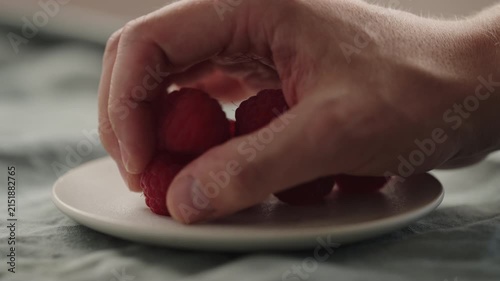 Slow motion man hand put fresh ripe raspberries on a white saucer