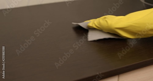 Home cleaning process, dust wiped off the cabinet, hand in yellow gloves cleaning the cabinet with a cloth.