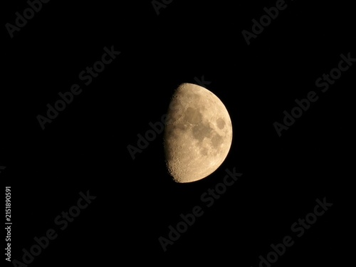 Fotografie Golden first quarter moon with craters details on black sky background