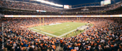 Fully blurred professional football stadium packed with spectators, soft floodlights and a distant green field creating an energetic sports atmosphere for advertising, tournaments and marketing.