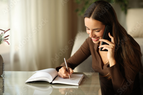 Happy woman writing in a paper agenda making phone call