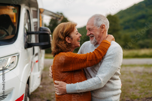 Принти на полотні Happy senior couple embracing beside camper during RV vacation.