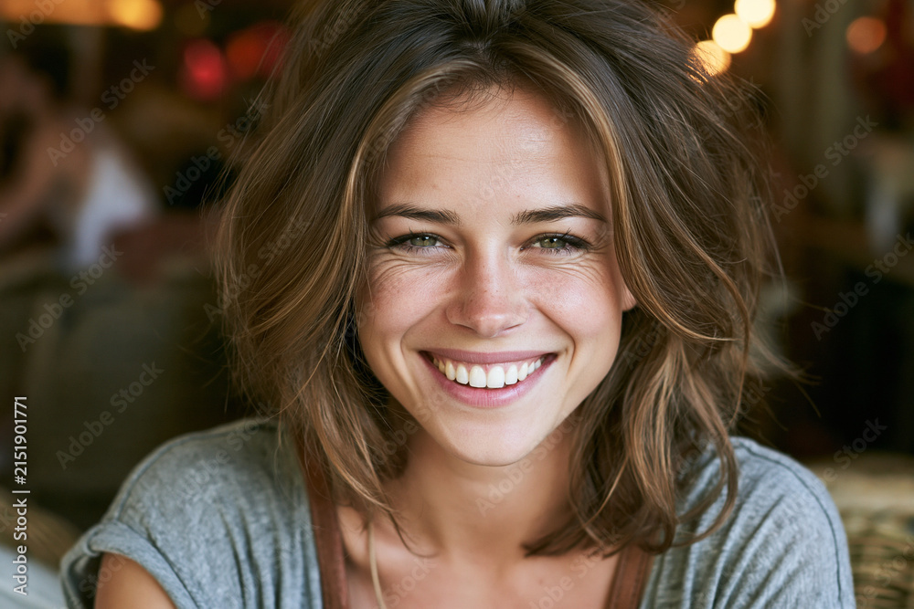 Obraz premium Woman smiles in a casual cafe setting with warm lighting and soft background