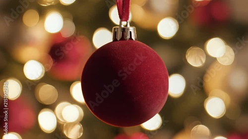 Red velvet christmas ornament hanging on festive tree with bokeh lights