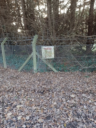Obraz na plátne Danger warning sign on security fence beside dense woodland