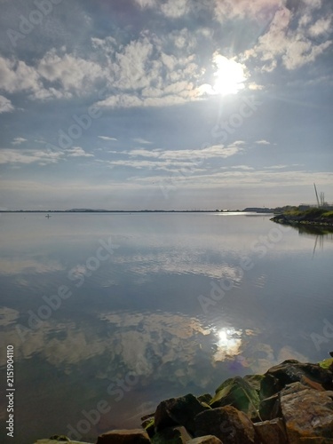 Konstfotografi Calm coastal water reflecting clouds beside a rocky shoreline