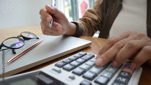 Professional business and financial planning concept featuring an entrepreneur working with a laptop, calculator, smartphone, and digital tablet at a wooden desk