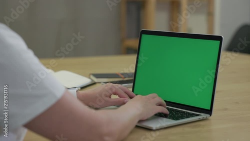 Woman Typing On Laptop Computer with Green Screen Chroma Key At Home Office Space. Female Freelancer Browsing Green Laptop Screen Using Keyboard and Touchpad
