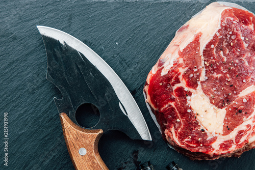 Fotografie Fresh cut steak with a unique knife on a dark stone surface
