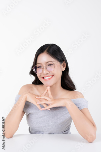 Happy young Asian woman smiling with fingers touching chin and wearing glasses on white background.