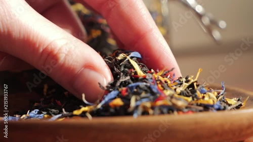 Close-up of female fingers picking up colorful loose leaf herbal tea from a wooden bowl. Assorted dried flowers and botanical ingredients for healthy natural tea preparation. High quality 4k footage