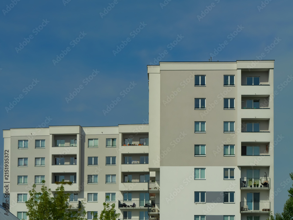 Fototapeta premium Modern white apartment building with balconies and geometric facade under a clear blue sky, representing contemporary urban housing, real estate and residential development