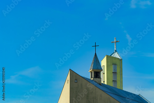 Modern Christian church roof and two crosses rising against a vivid blue sky, creating a minimalist religious scene with generous copy space for faith-based designs
