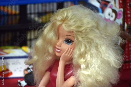 Hair styling doll head displayed among second hand objects at a flea market, representing a vintage beauty toy associated with childhood and creative play.
