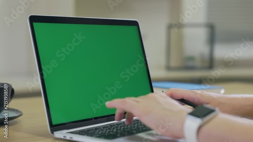 Woman Working On Laptop Computer with Green Mock Up Screen At Home Office Space. Female Freelancer Browsing Green Laptop Screen Writing Information in Notebook