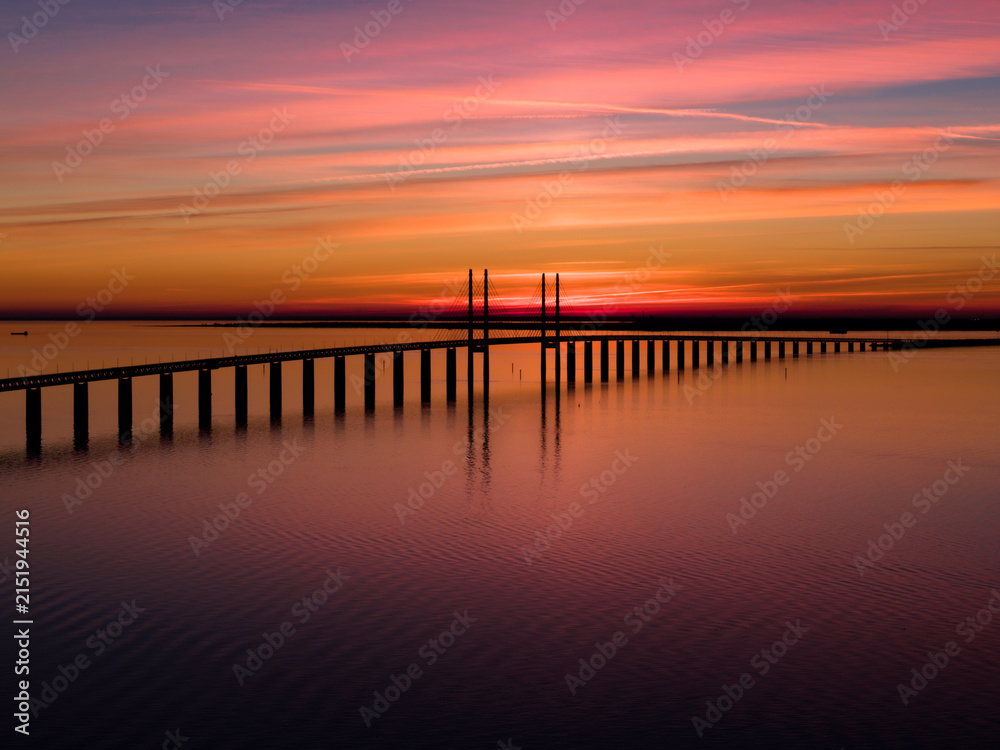 Fototapeta premium Scenic view of the Öresund Bridge connecting Sweden and Denmark, photographed from the Malmö side during a vivid colorful sunset over the Öresund Strait.