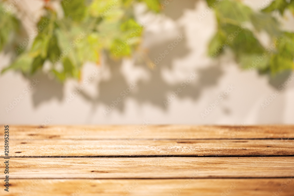Obraz premium Empty wooden table with blurred grape leaves and soft shadows as rustic autumn product background