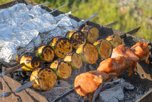 Delicious shish kebab and zucchini grilling on skewers over hot coals in a backyard grill. Meat and vegetables cooking outdoors during a sunny weekend picnic, preparing a tasty meal for family