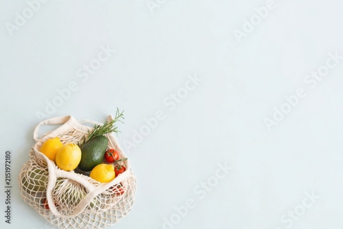 Fresh Organic Produce in Reusable Mesh Bag on Light Blue Background.